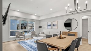 A modern living room with a large window, a dining table, and a chandelier. - 2 Bed/2 Bath Sparrowhawk-Courtyard Facing-Sleeps 6 (Dead Man's Flats)
