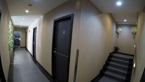 A hallway with doors, a staircase, and a plant. - Nine Days Hotel (Batam)