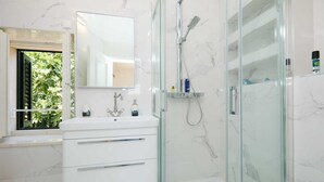 A modern bathroom with a glass-enclosed shower, a white marble sink, and a large mirror. - Karma Suites by Dominium Comfort double room (Dubrovnik)