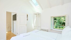 A bedroom with a skylight, a window with a view of greenery, a bed with white linens, and a wardrobe. - Karma Suites by Dominium Comfort double room (Dubrovnik)