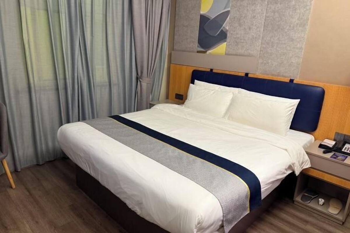 A hotel room with a bed, a nightstand, a chair, and a window with curtains.
