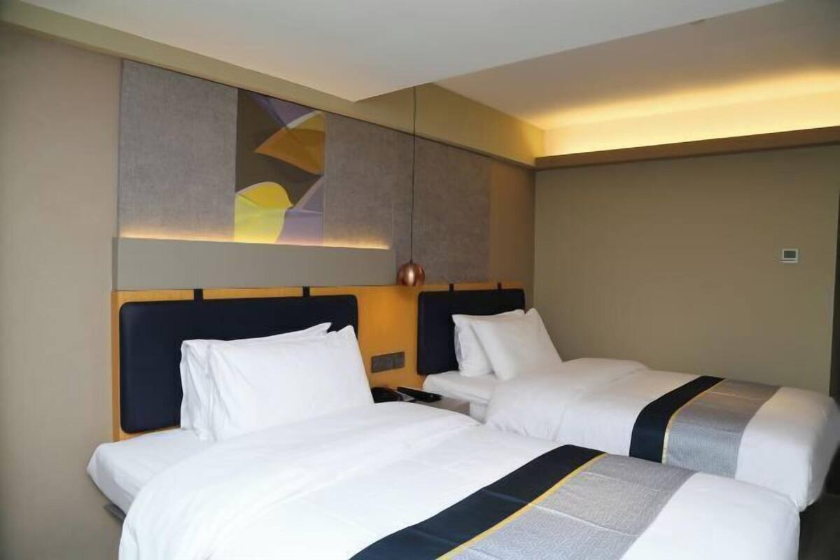 A hotel room with two beds, a modern headboard, a wall-mounted artwork, and a ceiling light fixture.
