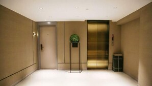 A modern elevator with a metallic finish, a small potted plant on a stand, and a trash bin to the right. - Homeinn Selected Hotel (Beijing Normal University Jishuitan Subway Station) (Beijing)