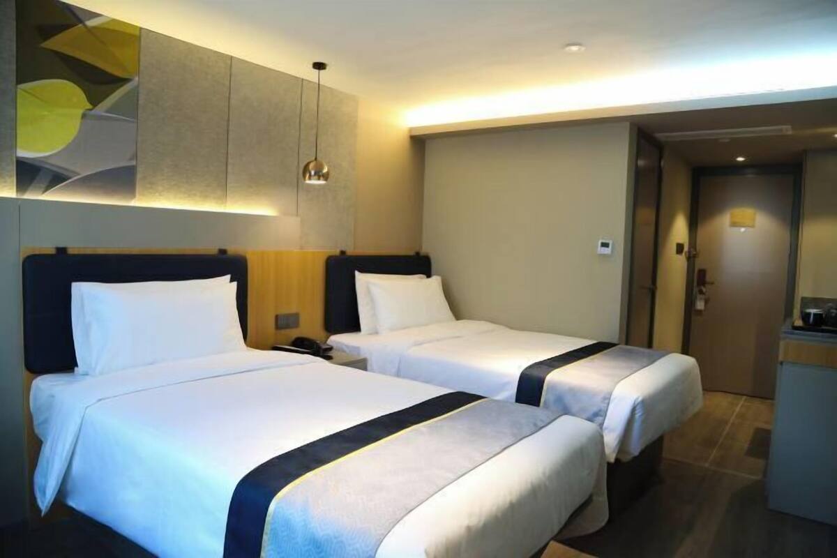 A hotel room with two beds, a small desk, and a wall-mounted artwork.