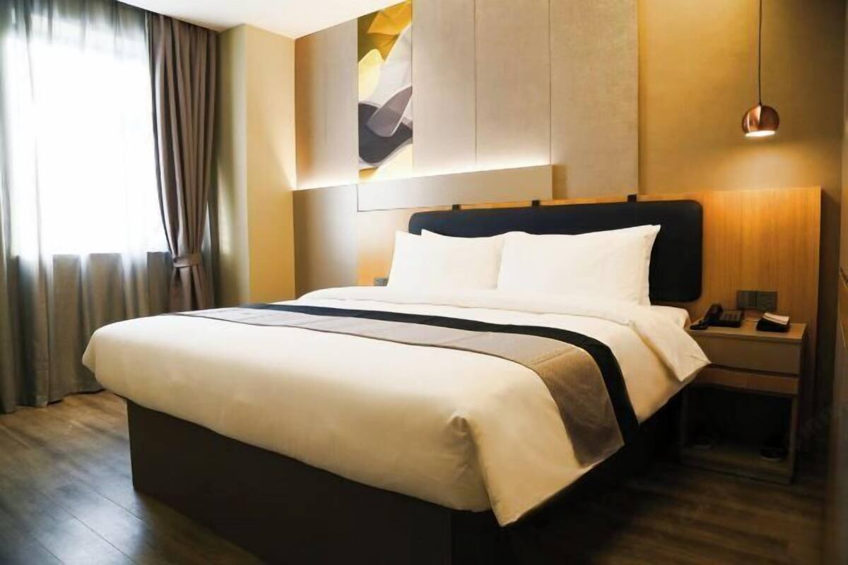 A hotel room with a large bed, a bedside table, a lamp, and a painting on the wall.
