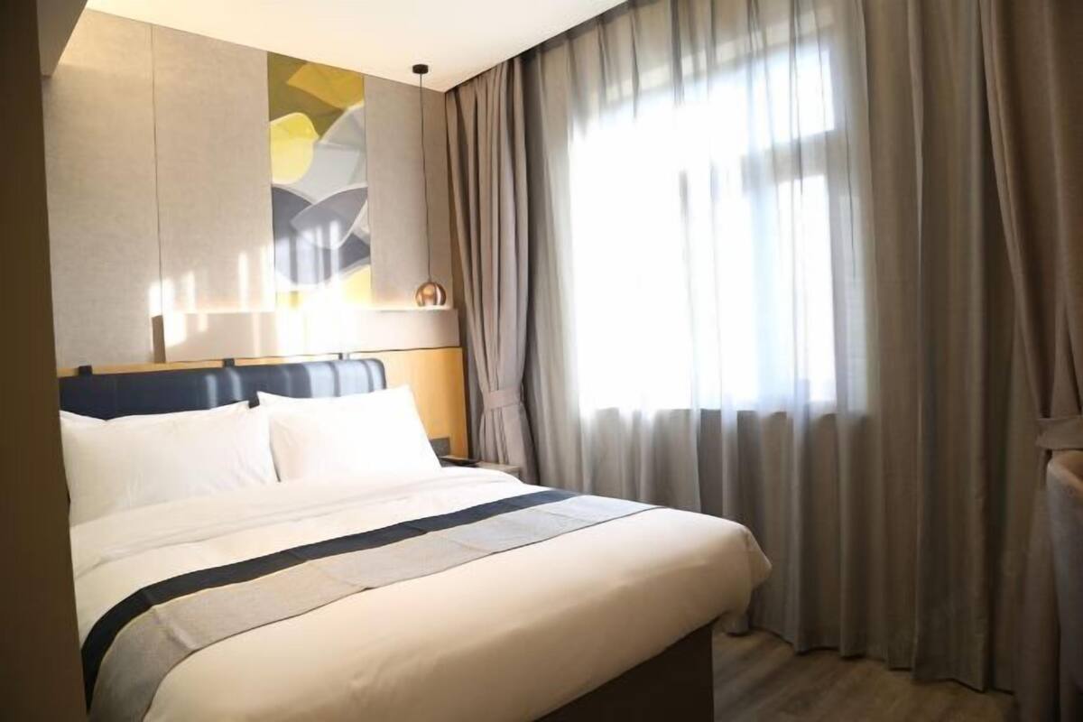 A hotel room with a bed, curtains, a wall art piece, and a window.