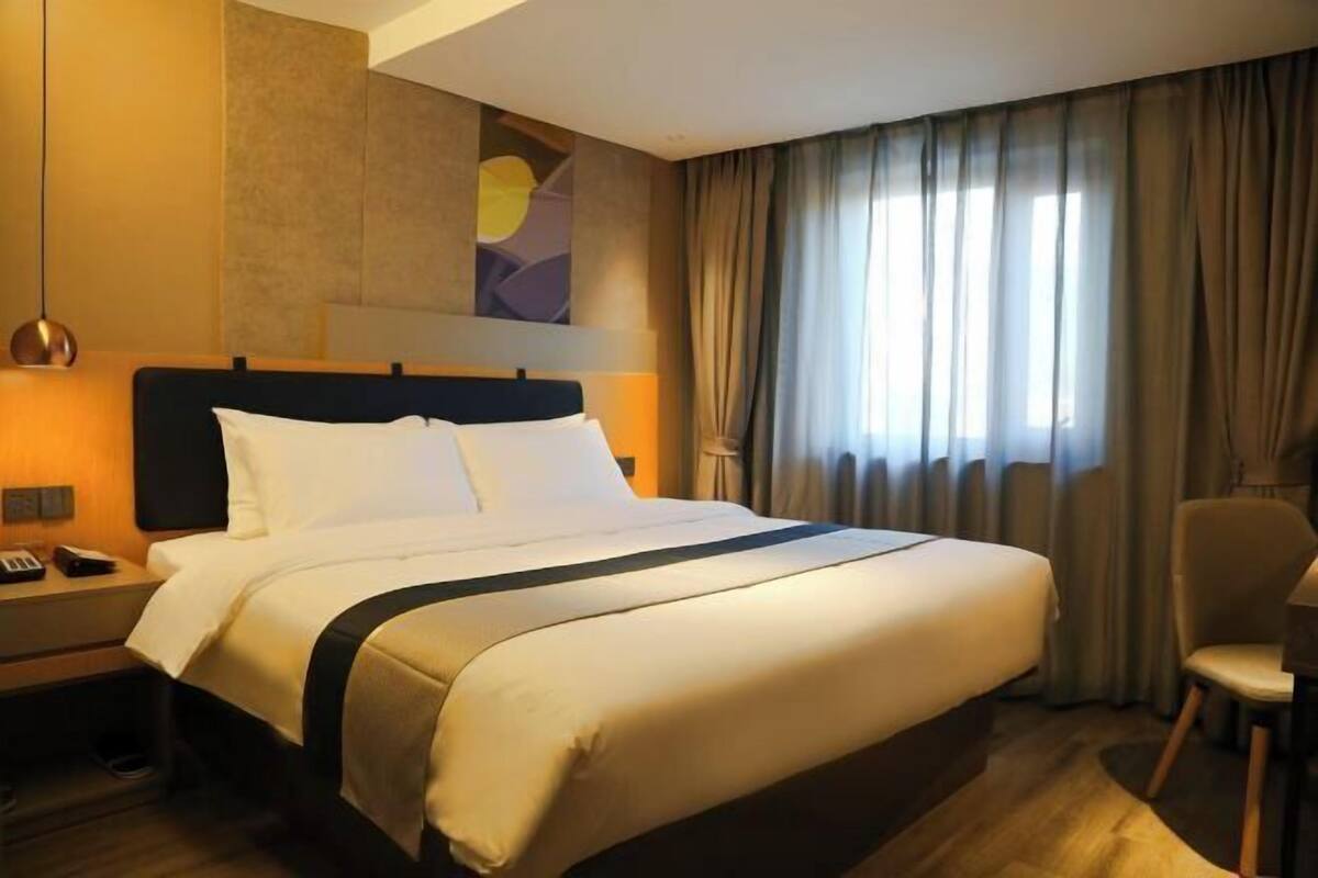 A hotel room with a large bed, a nightstand, a chair, and a painting on the wall.