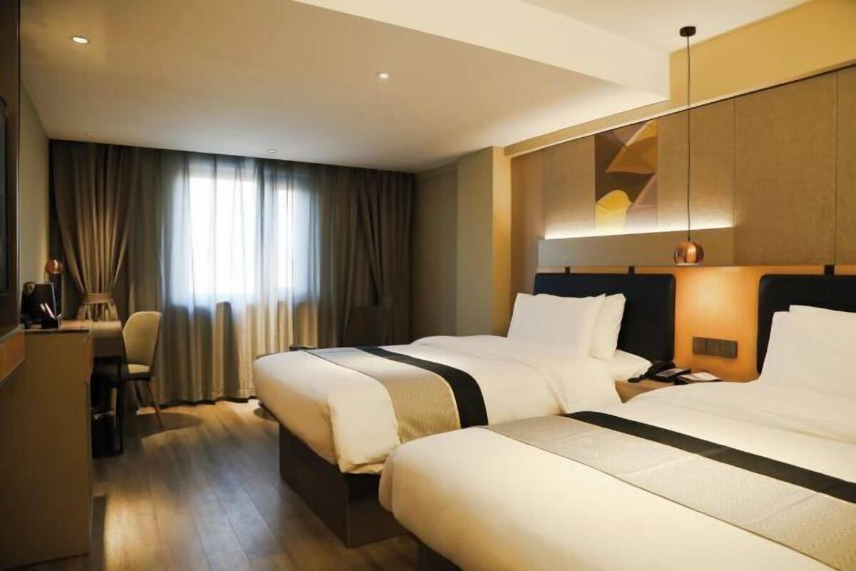 A hotel room with two beds, a desk, a chair, and a large window with curtains.