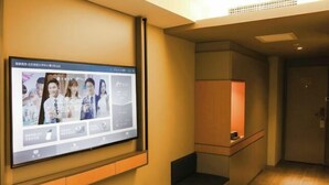 A hotel room with a large flat-screen TV mounted on the wall, a small seating area with a cushioned bench, and a wooden cabinet with a lamp. - Homeinn Selected Hotel (Beijing Normal University Jishuitan Subway Station) (Beijing)