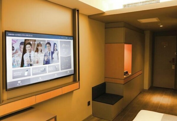 Ein Hotelzimmer mit einem großen Flachbildfernseher an der Wand, einer kleinen Sitzecke mit gepolstertem Sitz und einer Holzkabine mit Lampe.