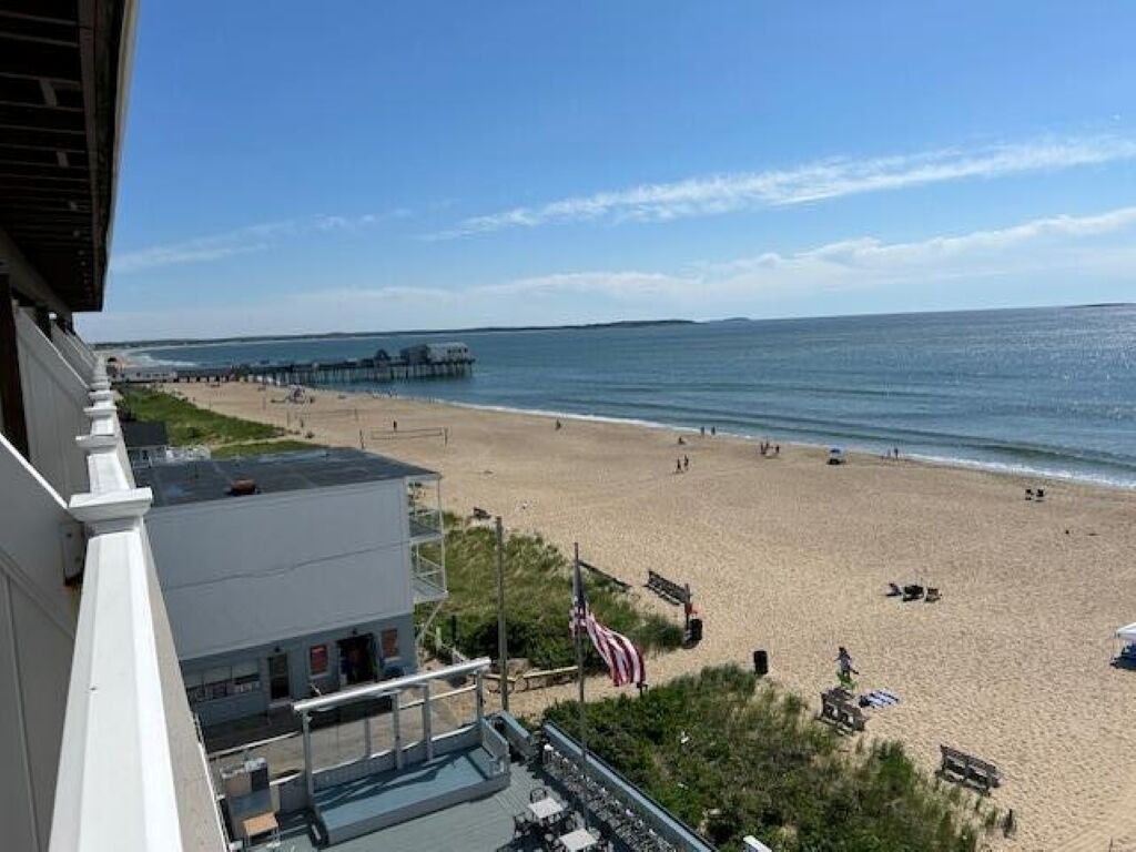 A beach view from a building with a balcony, a pier in the distance, and a flag on the beach.