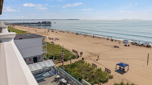 A beach with a pier, beach umbrellas, and a building with outdoor seating.