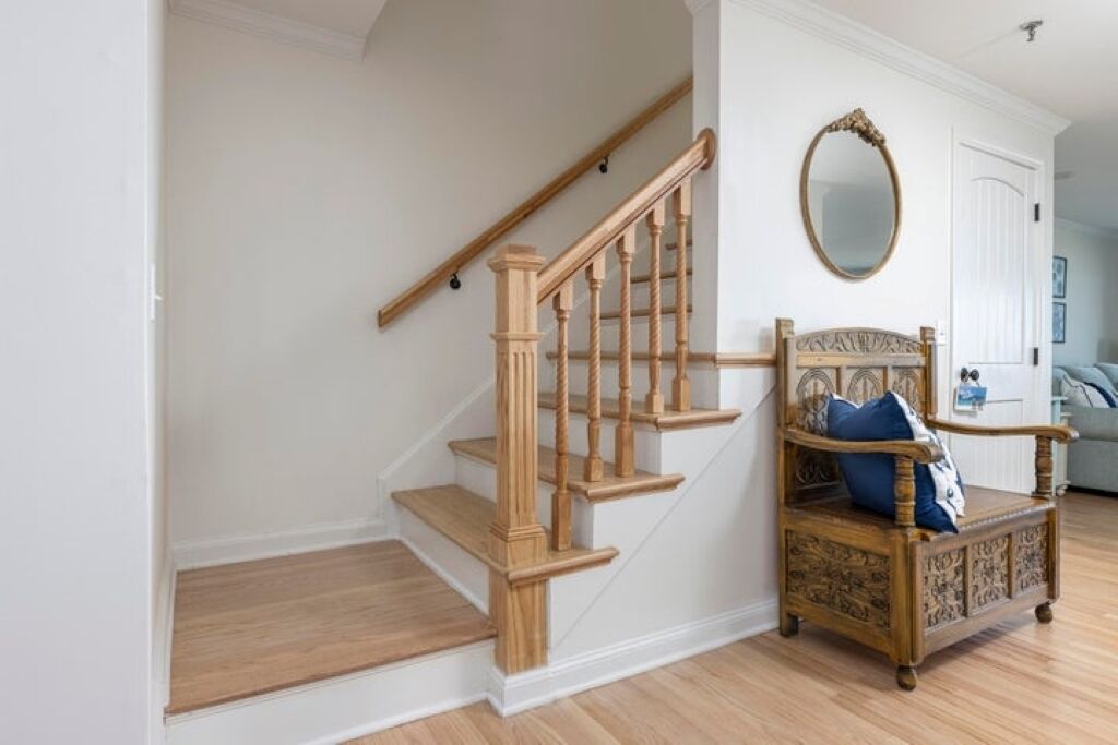 A staircase with wooden steps and balusters, a chair with a decorative backrest, and a round mirror on the wall.