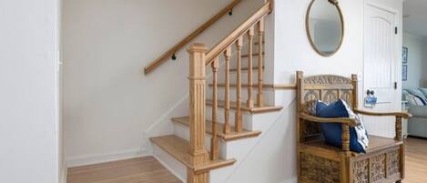 A staircase with wooden steps and balusters, a chair with a decorative backrest, and a round mirror on the wall.
