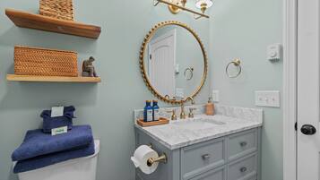 A bathroom with a marble sink, a round mirror with a gold frame, and wooden shelves with baskets.