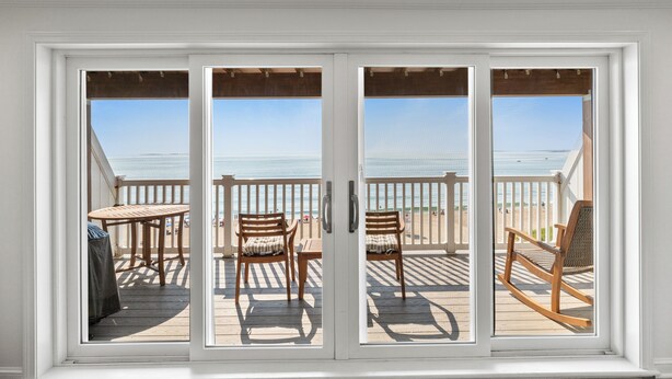 A balcony with a view of the beach, wooden furniture, and a table.