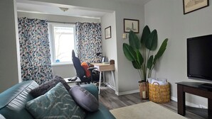 Un salon comprenant un canapé, un bureau avec une chaise, un téléviseur et une grande plante.