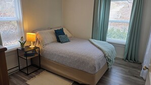Une chambre à coucher avec un lit, une table de chevet, une lampe et des fenêtres avec des rideaux.