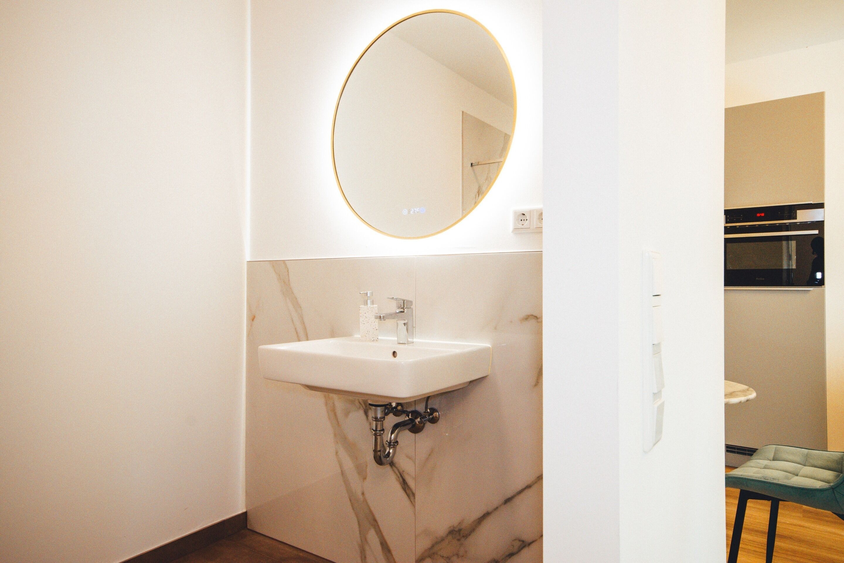 A bathroom with a white sink, marble walls, and a round mirror.