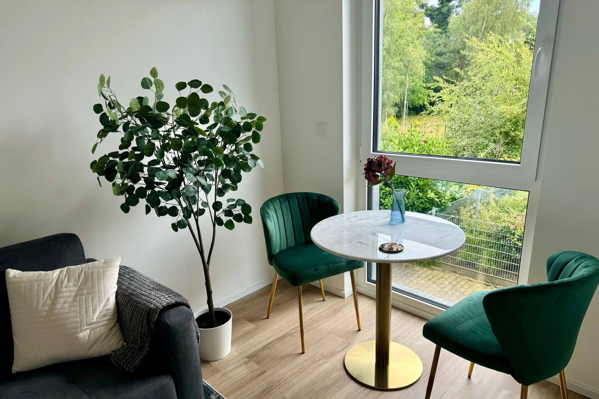Un salon moderne avec un canapé vert foncé, une table ronde en marbre et une plante en pot.