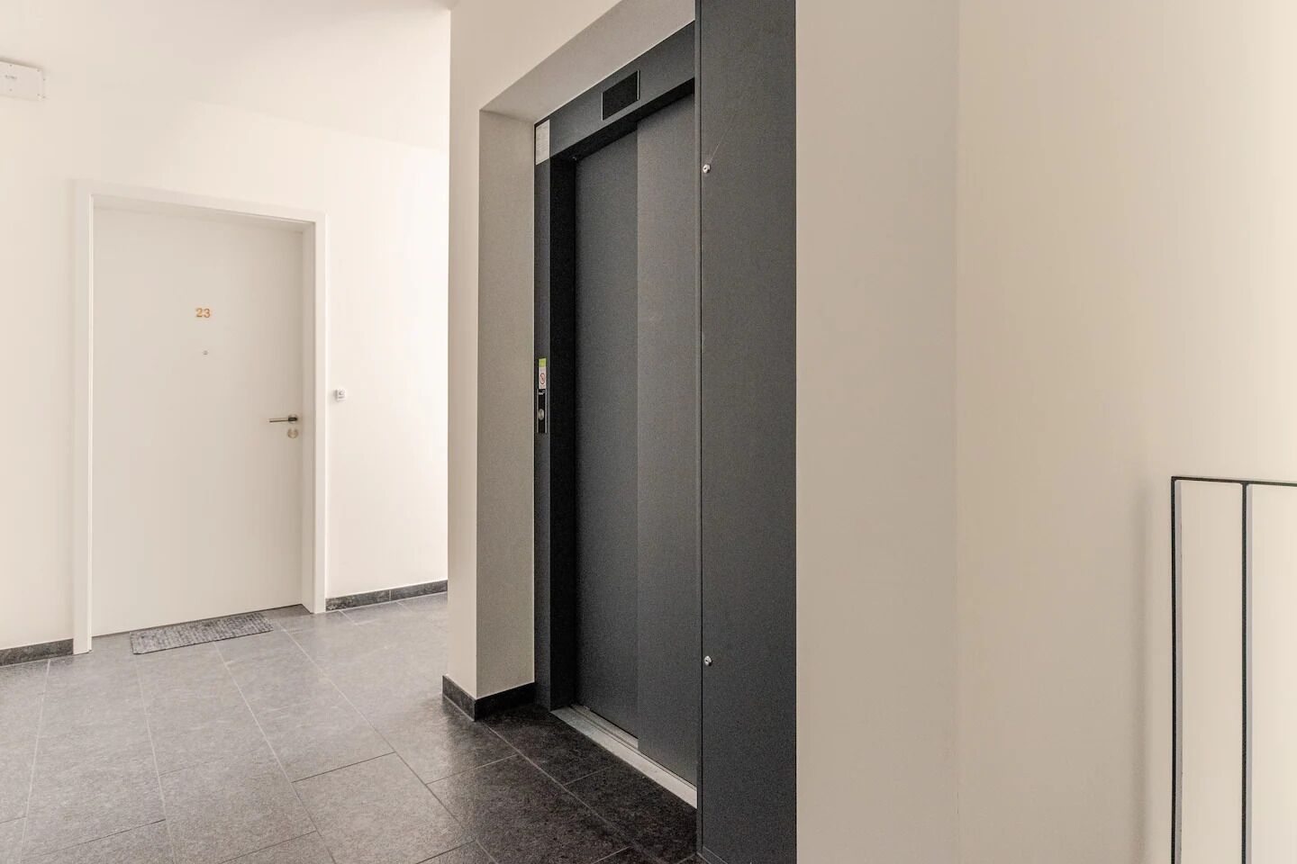 A hallway with a door marked '23' and a modern elevator.
