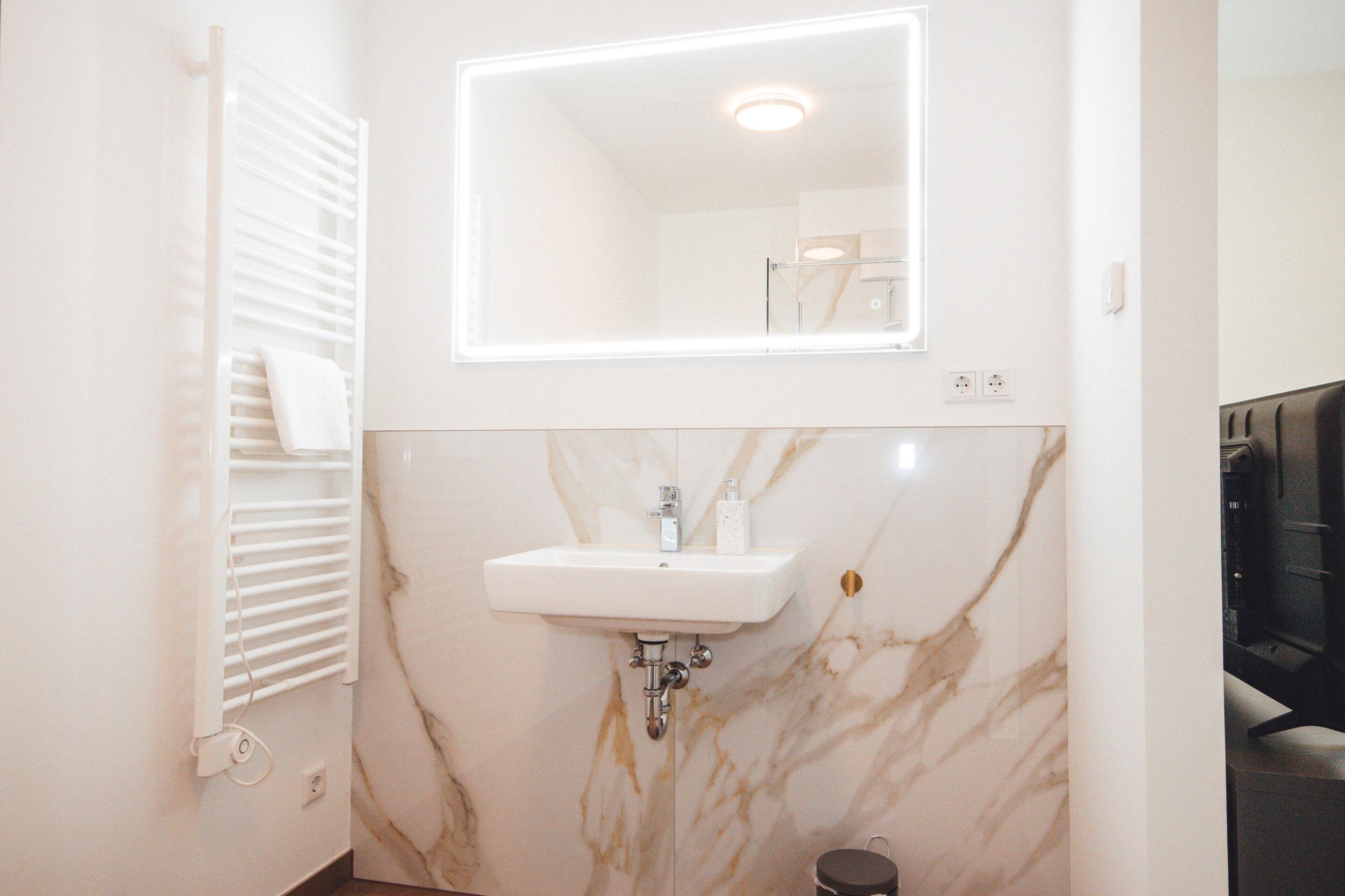 A bathroom with a white sink, marble walls, and a mirror above it.