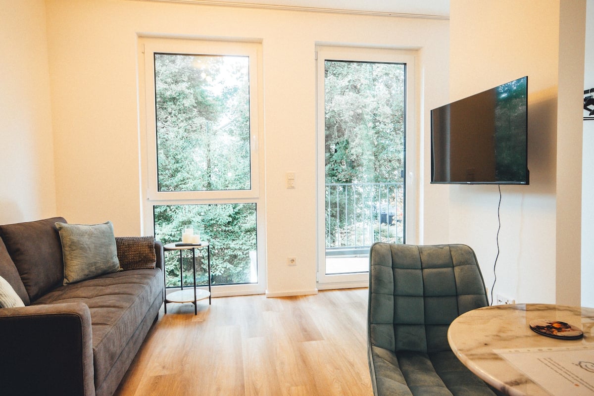 Un salon moderne avec un canapé, un fauteuil, une petite table et un téléviseur fixé au mur.