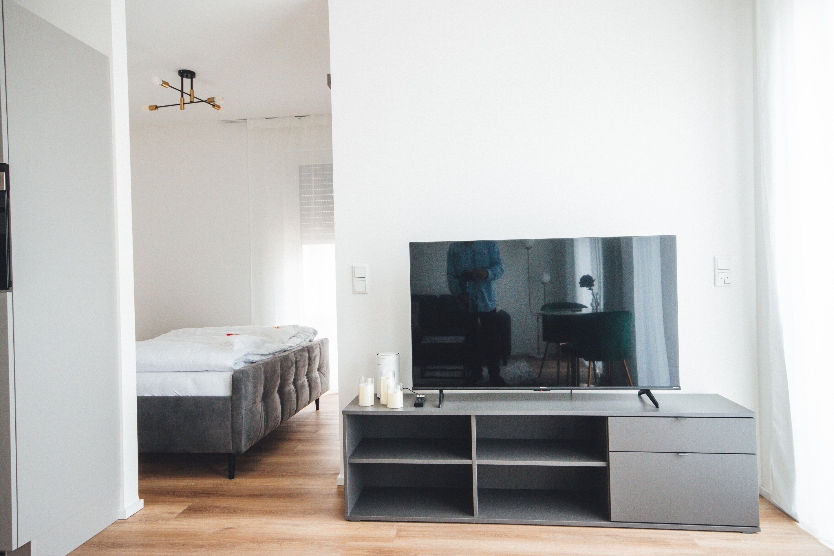 Una sala de estar moderna con un televisor de pantalla plana grande sobre un mueble gris, un sofá gris y piso de madera.