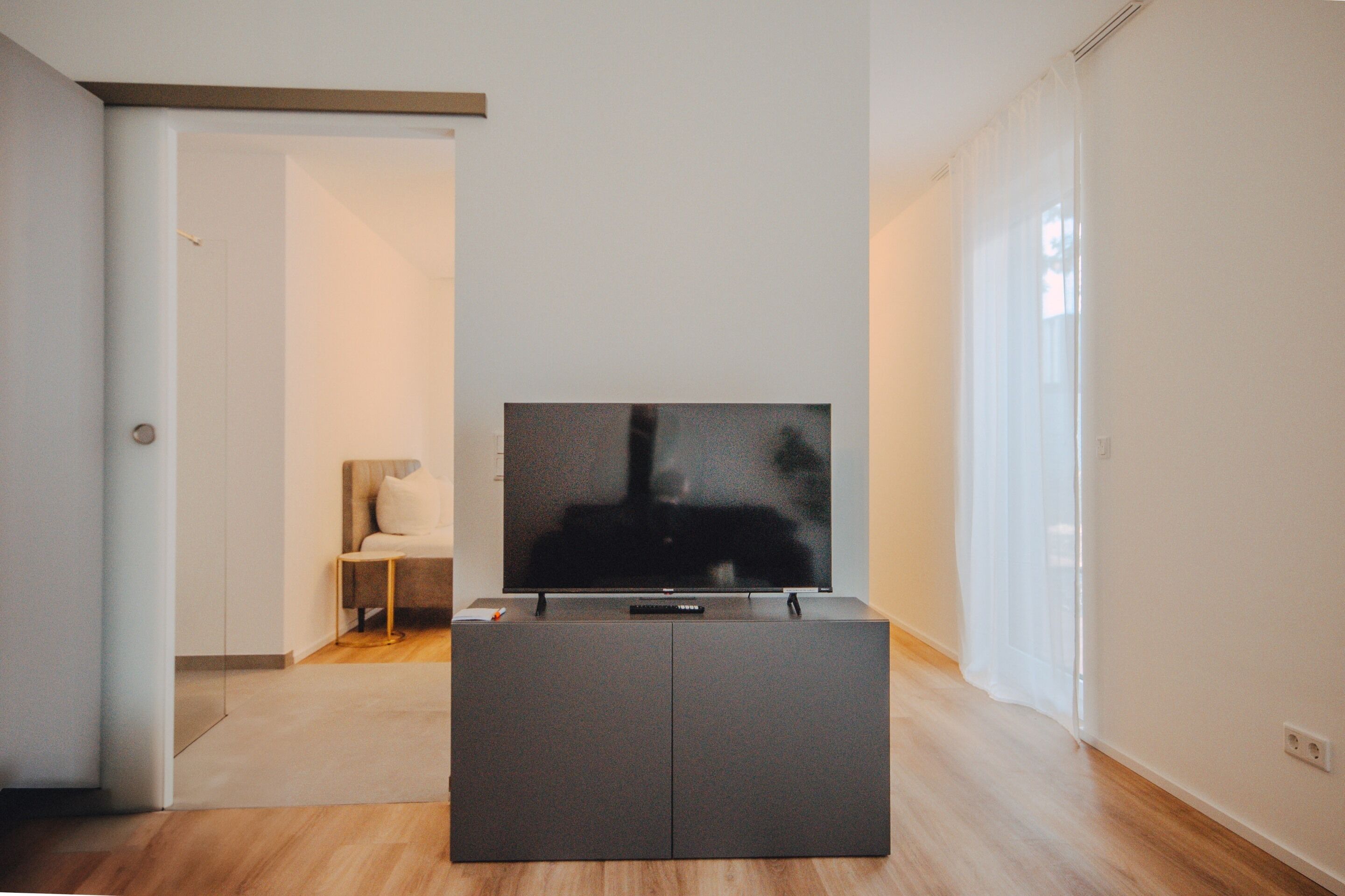 Un salon moderne avec un téléviseur à écran plat posé sur un meuble sombre, une petite table d’appoint et un fauteuil.