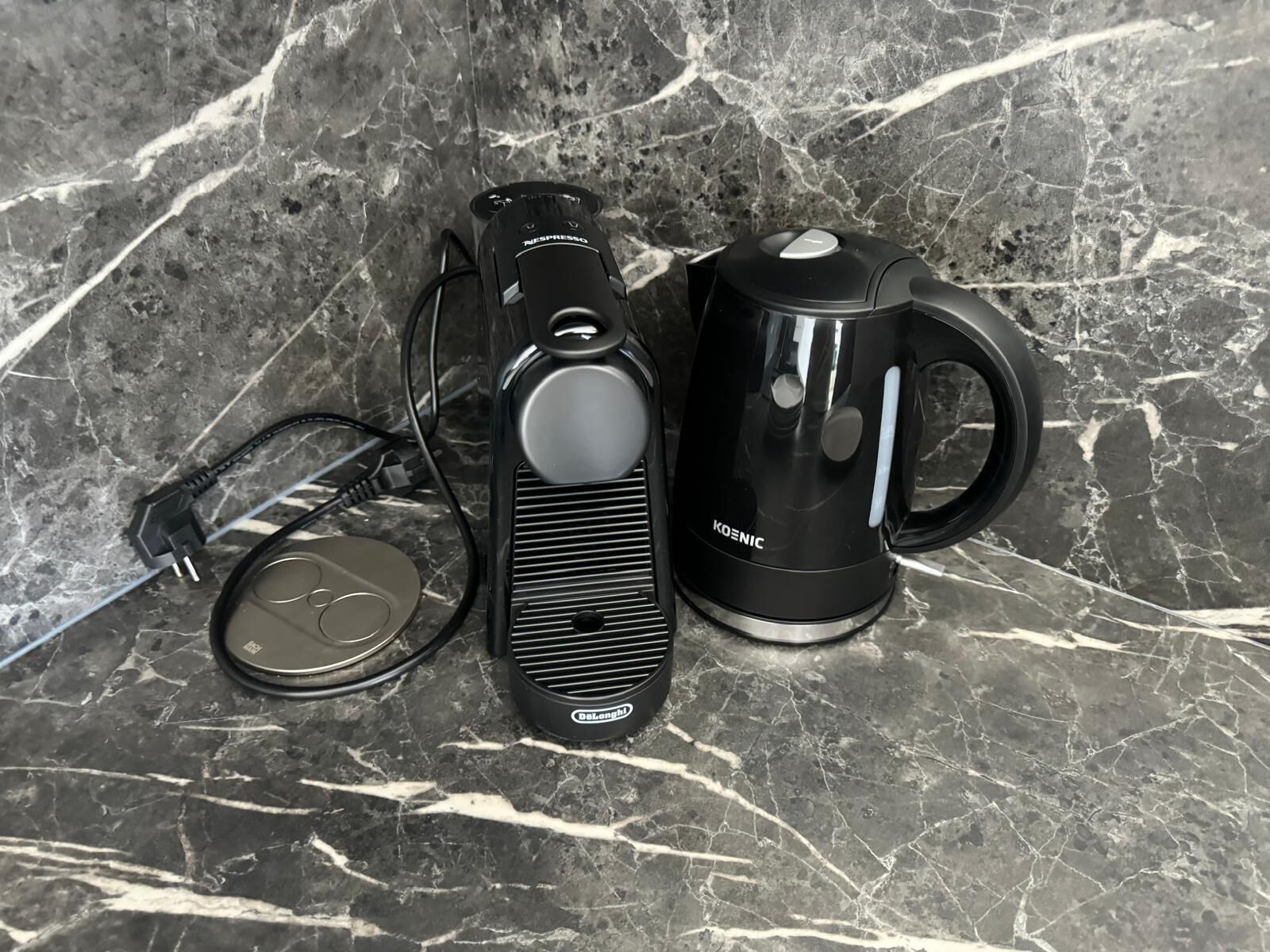 Eine Kaffeemaschine, ein Wasserkocher und ein Stromkabel auf einer Marmorarbeitsplatte.