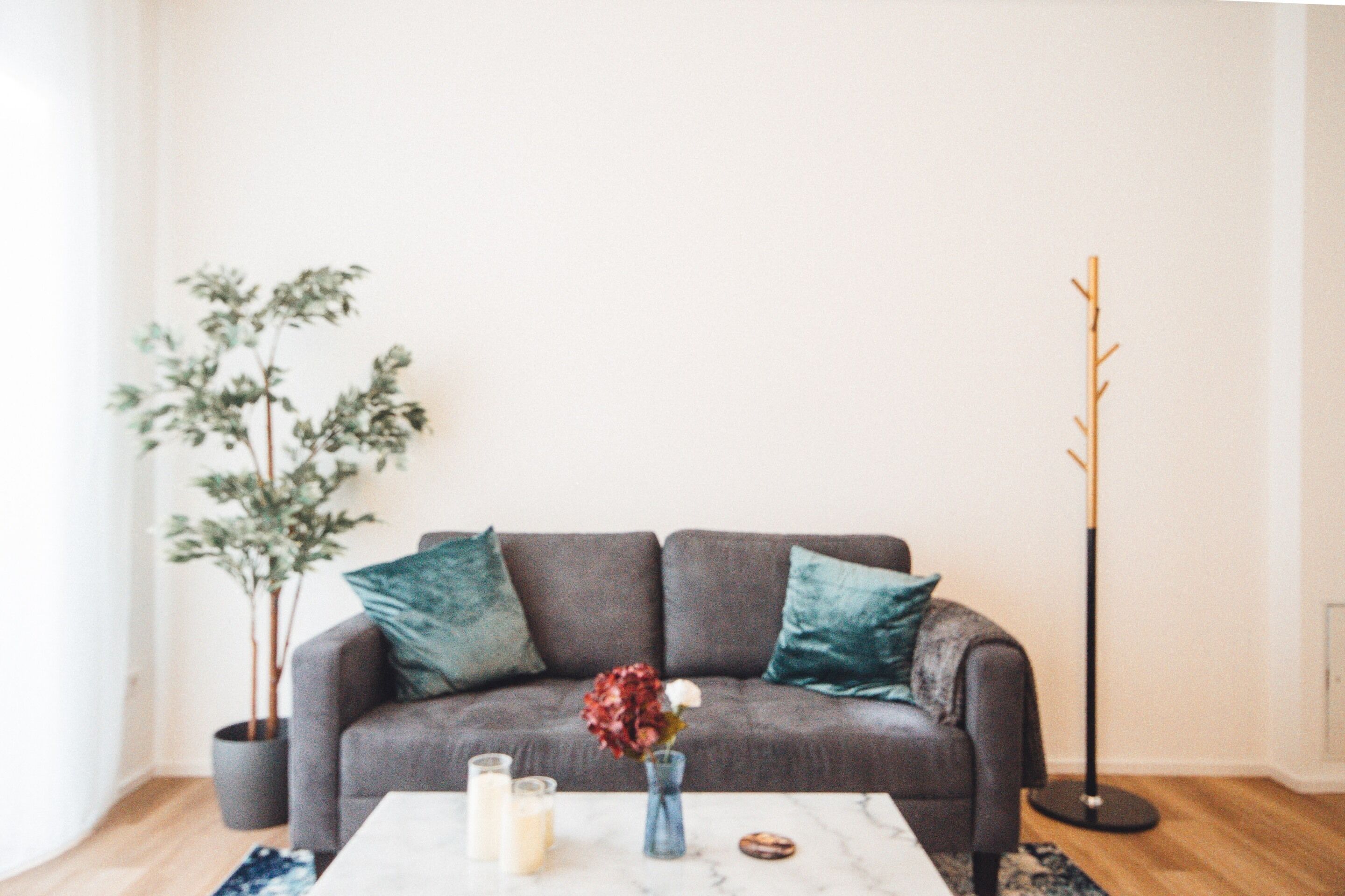 Un salon moderne avec un canapé gris, des coussins turquoise, une table basse avec des bougies, un vase de fleurs, une plante en pot et un lampadaire.