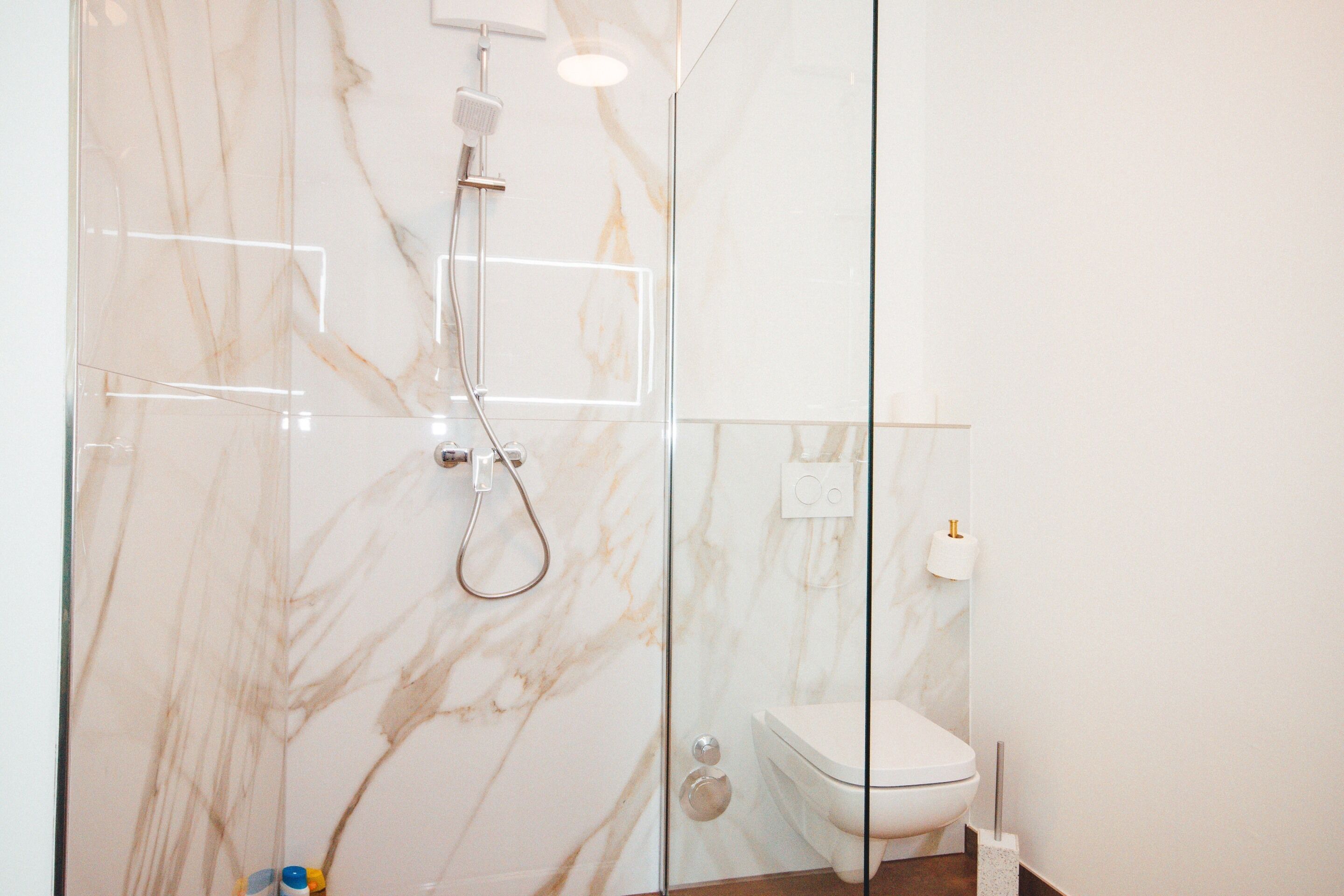 A modern bathroom with a glass shower enclosure, a toilet, and marble walls.