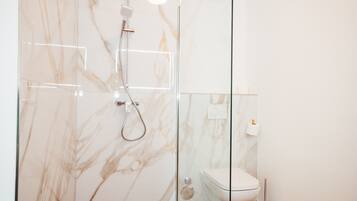 A modern bathroom with a glass shower enclosure, a toilet, and marble walls.