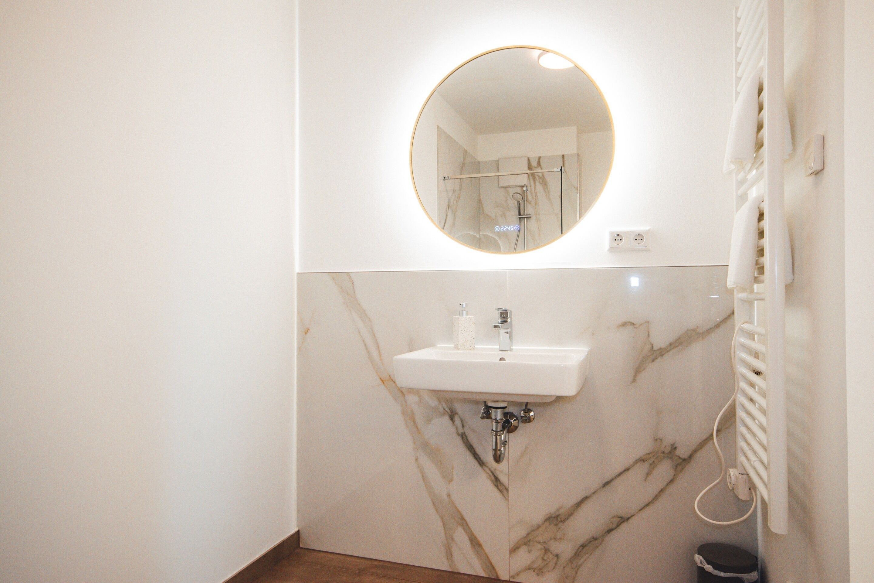 Une salle de bain avec un lavabo en marbre, un miroir rond et un porte-serviettes.