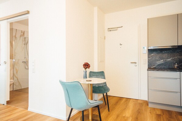 Cocina compacta con encimera de mármol, un pequeño comedor con dos sillas y una puerta blanca.