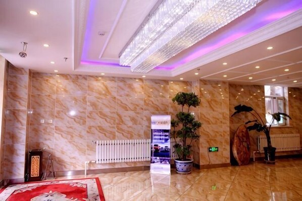 A lobby with marble walls, a large chandelier, potted plants, and a reception desk.