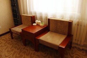 A hotel room with a wooden table and two upholstered chairs, a small side table with a few items, and a window with sheer curtains. - Yake Shiyuxin Business Hotel (Yakeshi)