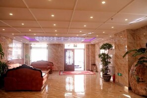 A hotel lobby with a marble floor, a reception desk, a red carpet, and a potted plant. - Yake Shiyuxin Business Hotel (Yakeshi)