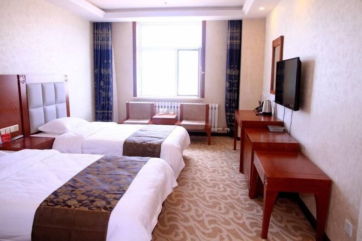A hotel room with two beds, a small sofa, a desk, a television, and a window with curtains.