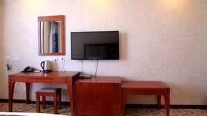 A hotel room with a wooden desk, a television mounted on the wall, a small cabinet, and a mirror. - Yake Shiyuxin Business Hotel (Yakeshi)