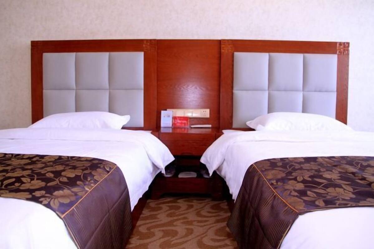 A hotel room with two beds, a wooden headboard, and a nightstand with a red object.