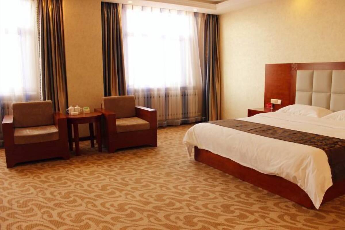 A hotel room with a large bed, two armchairs, a small table, and a nightstand.