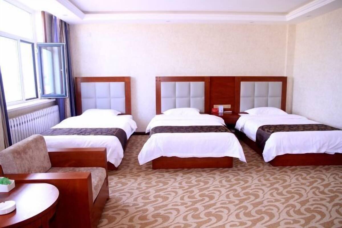 A hotel room with three beds, a round wooden table, and a window with curtains.