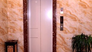 An elevator with a marble wall, a control panel, and a potted plant. - Yake Shiyuxin Business Hotel (Yakeshi)