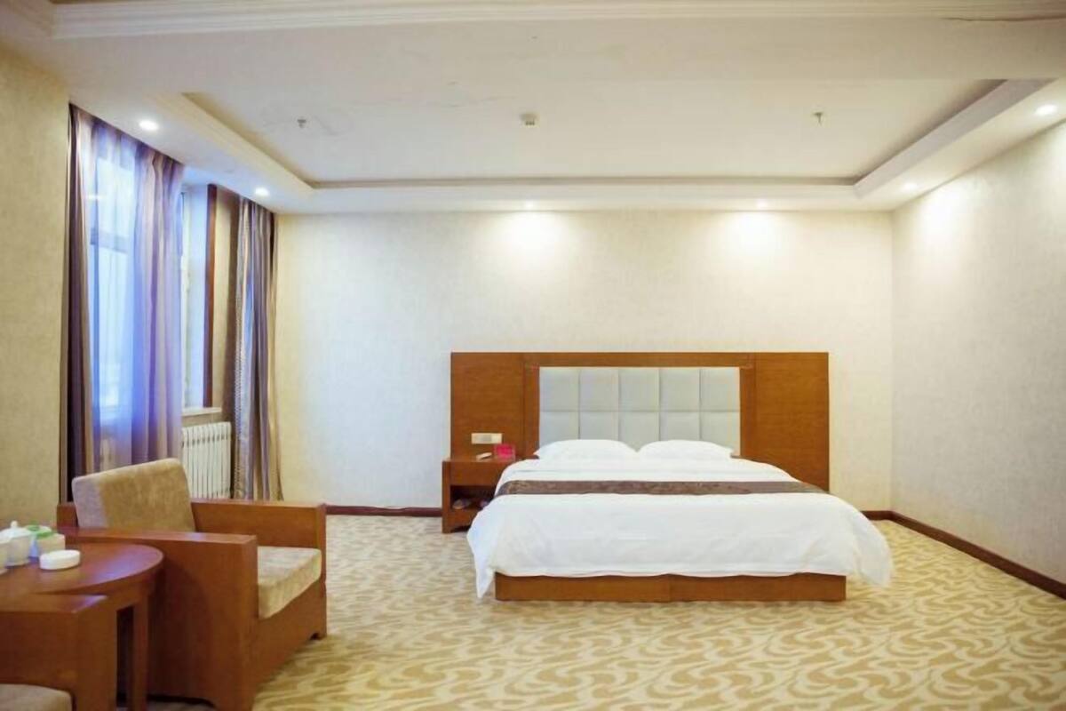 A hotel room with a bed, a chair, a small table, and a nightstand.