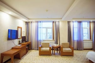 Una habitación de hotel con una cama, dos sillones, una mesita, un televisor y una ventana con cortinas.