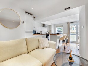 Una sala moderna con un sofá, una mesa de centro de vidrio y una cocina al fondo.