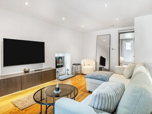 A modern living room with a large flat-screen TV, a sofa, a coffee table, and a small side table.