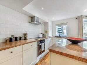 A modern kitchen with white cabinetry, a granite countertop, a stainless steel range hood, and a large window with a view of a stone wall and a wooden deck. - 1 bedroom accommodation in Bowness-on-Windermere (Bowness-on-Windermere)
