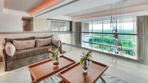 A modern living room with a sofa, two coffee tables, and large windows offering a view of greenery.